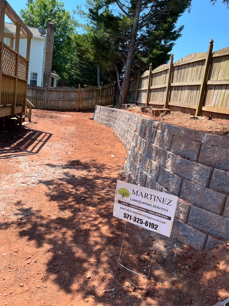 Newly built block retaining wall holding back a graded slope beside a fence