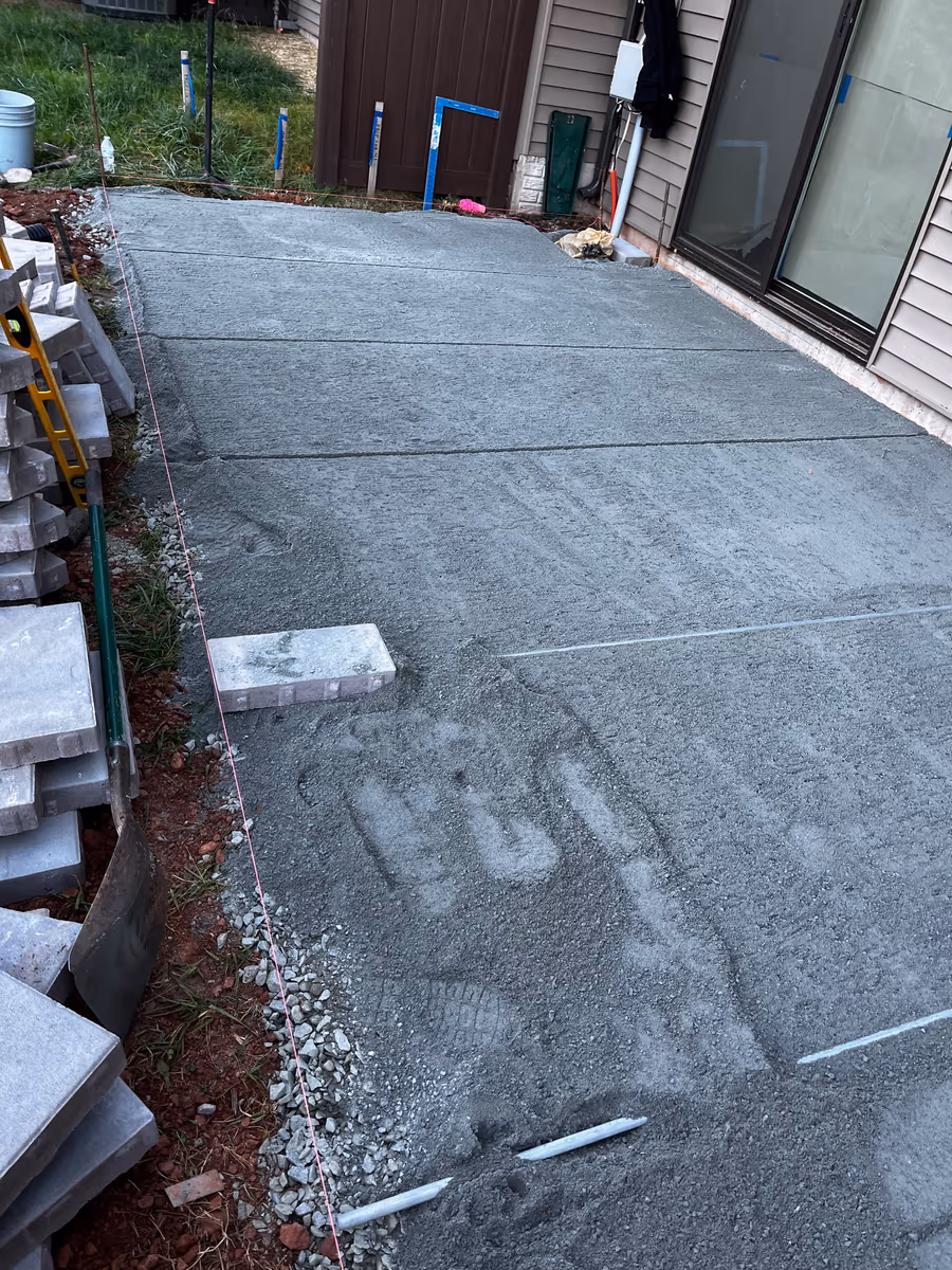 Freshly poured and floated concrete slab with paving materials stacked alongside