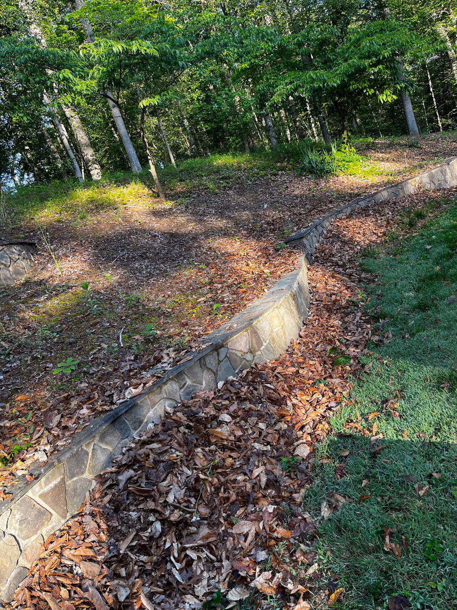 Planting bed buried under fallen leaves along a stone wall before a fall clean-up