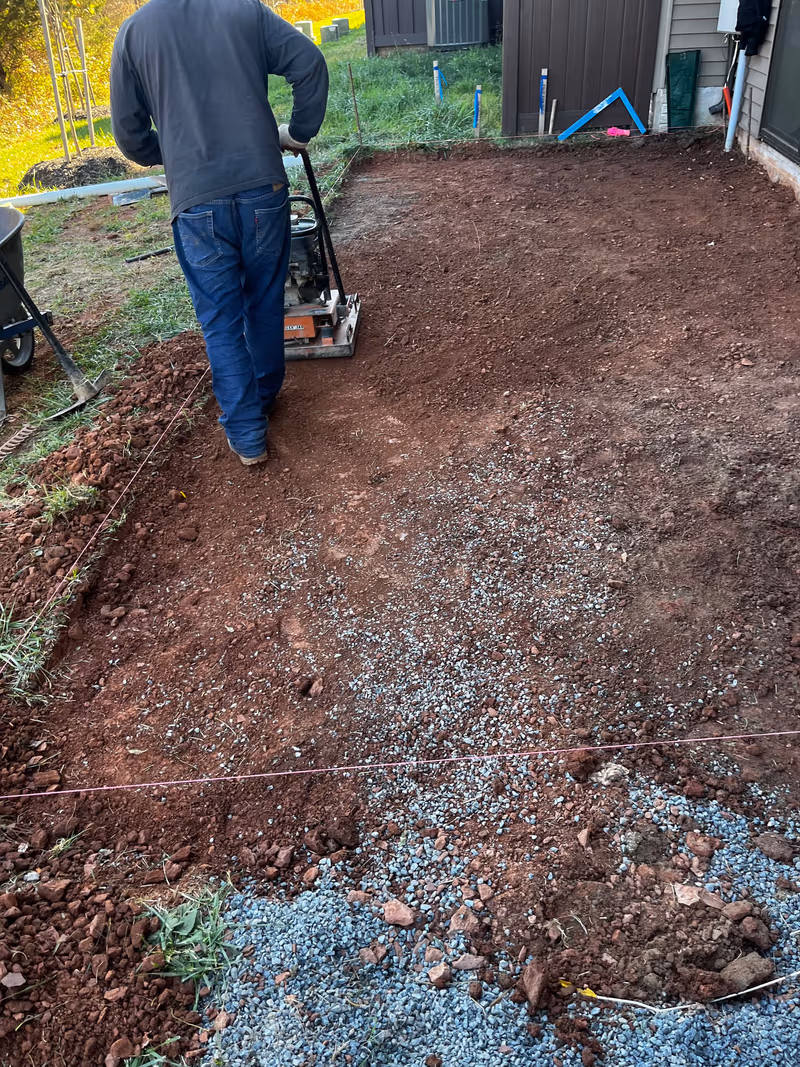 Crew member running a plate compactor over the gravel base of a new patio