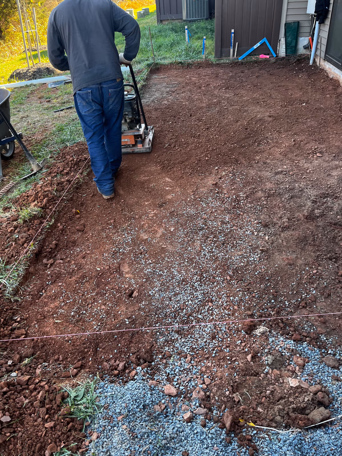 Crew member running a plate compactor over the gravel base of a new patio