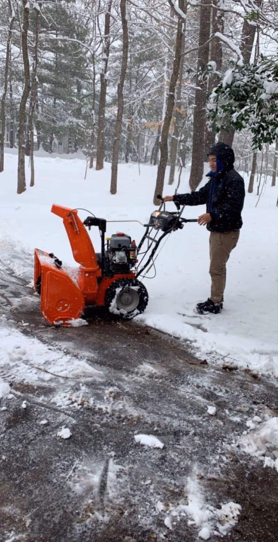 Operator clearing a snow-covered driveway with a walk-behind snow blower