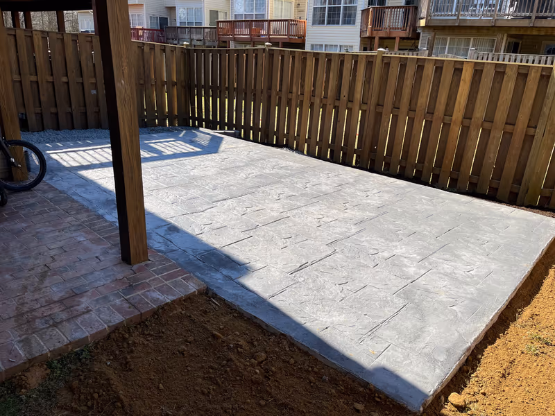 Stamped concrete patio finished beneath a raised deck, edged in brick